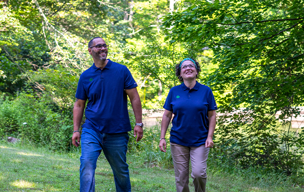 a man and a woman adult volunteer in blue shirts walking through nature
