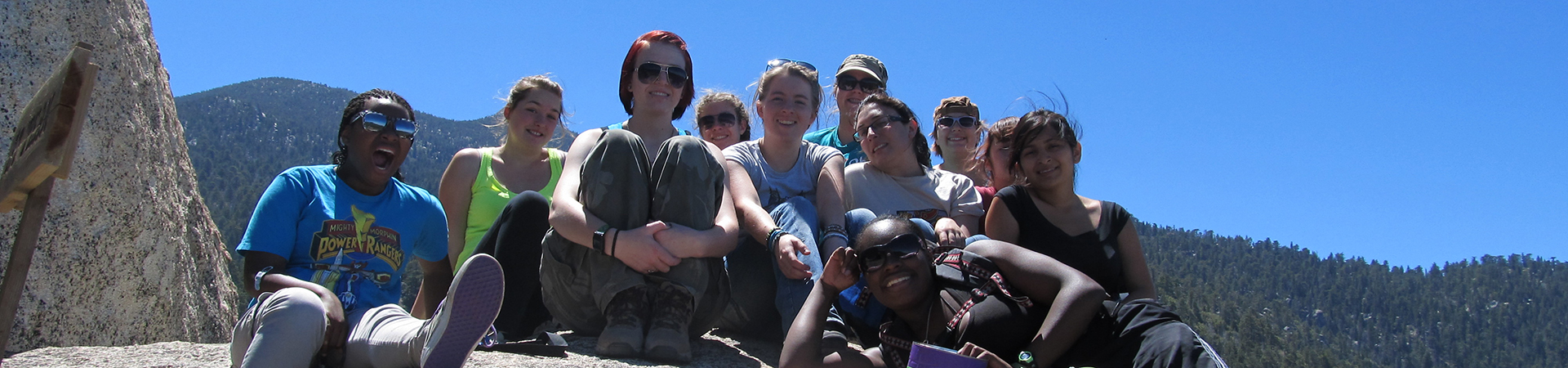  large group of older girls sitting on a boulder with the mountain valley in the background 