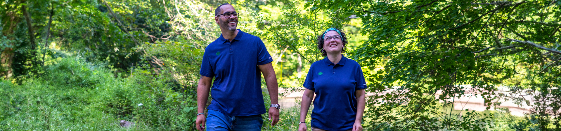  a man and a woman adult volunteer in blue shirts walking through nature 