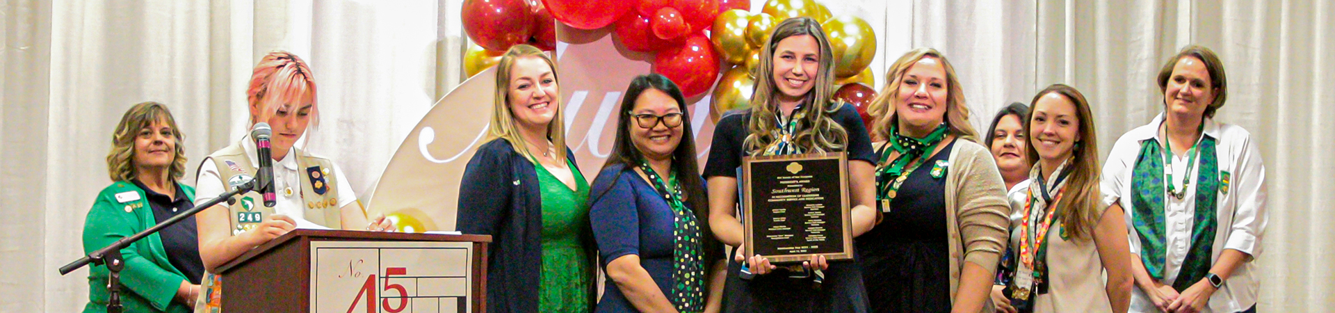  image of woman receiving award with other women and older girl scouts lined up behind her on a stage 